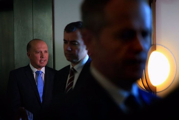 Immigration Minister Peter Dutton stands in the corner in the spotlight as bill shorten and another mp walk away from him