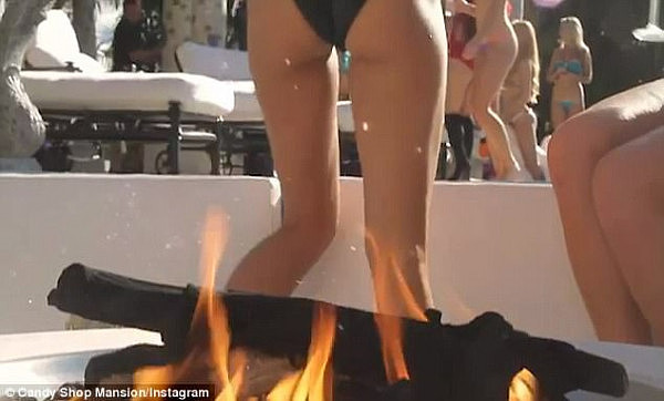 The lady is seen dancing while holding a champagne glass in front of an open fire pit