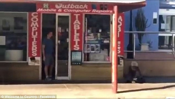 The footage shows an Aboriginal man sitting on the ground next to two businesses- Darwin Tours and Darwin Fishing Office 
