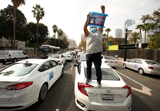 2020年10月8日，洛杉矶，一名Uber司机站在车顶举着“NoonProp22”的牌子进行抗议图片来源：businessinsider