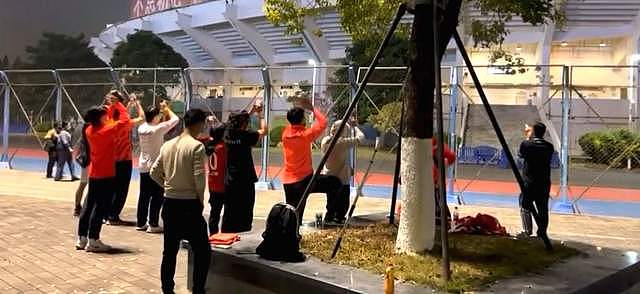 十几位广州队球迷在铁丝网外举着旗帜，高唱歌曲，路人一脸诧异 - 2