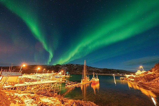 在挪威的小海湾，夜幕已悄然降临，绚丽的北极光在绿色和酒红色光芒中熠熠生光。